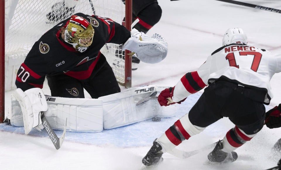 New Jersey Devils defenseman Simon Nemec, right, bends his stick as he tries to push the puck past Ottawa Senators goaltender Joonas Korpisalo, left, during second-period NHL hockey game action in Ottawa, Ontario, Saturday, April 6, 2024. (Adrian Wyld/The Canadian Press via AP)