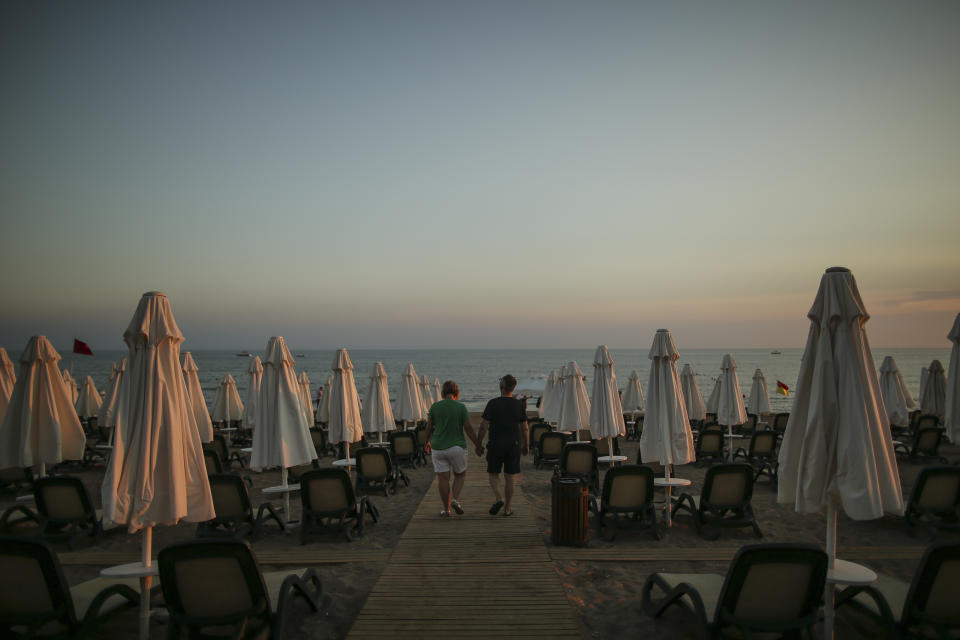 Tourists walk at the beach of Antalya, southern Turkey, as the sun sets, on Sunday, June 20, 2021. Hotels in Turkey's Antalya region, a destination beloved by holidaymakers, are preparing to finally resume operations as they expect the return of international tourists after months of setbacks caused by the pandemic that halted travel. (AP Photo/Emrah Gurel)