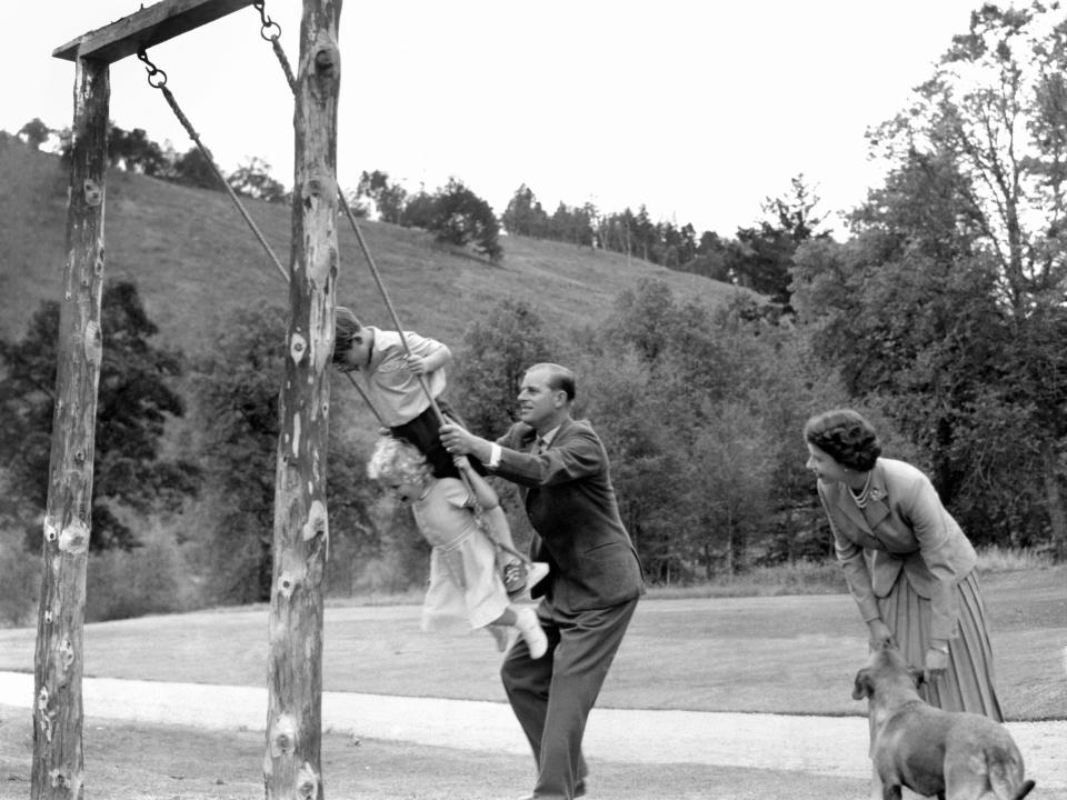 Prince Charles and Princess Anne being pushed on a swing by Prince Philip