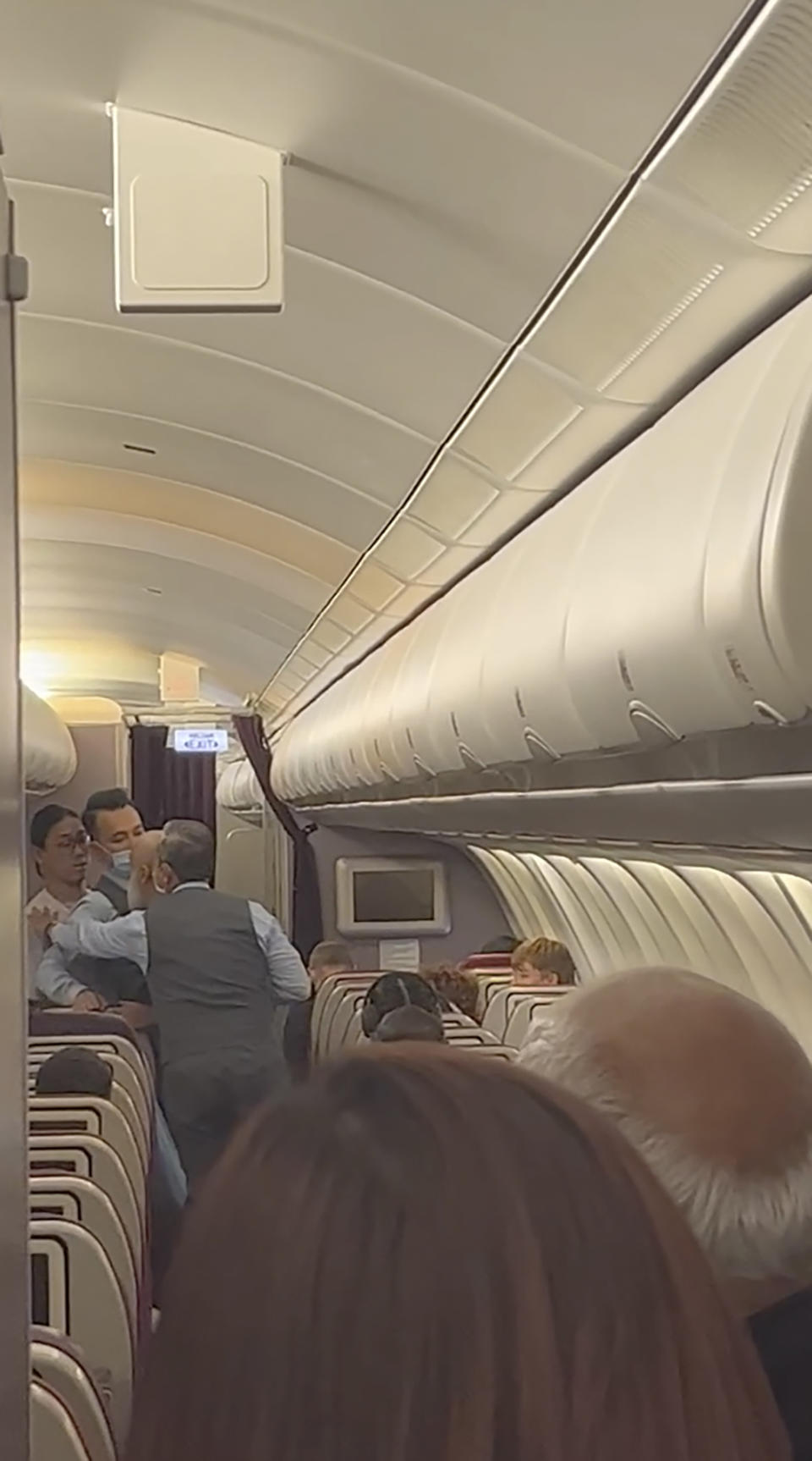 In this image taken from a video, a passenger standing in the aisle, second right, argues with crew members during a flight from Australia to Malaysia, Monday, Aug. 14, 2023. Malaysia Airlines flight MH122 returned on Monday to Sydney, where the passenger was arrested hours later in what police described as an emergency incident. (Velutha Parambath via AP)