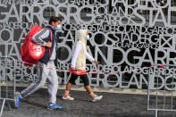 Serb's Natalija Kostic, right, and her coach Nicola Stevanovic wearing face masks to prevent the spread of coronavirus walk past a sign at at the Roland Garros stadium in Paris, Friday, Sept. 25, 2020. Already repeatedly trimmed, crowd sizes for the French Open have been reduced again to just 1,000 spectators per day because of the worsening coronavirus epidemic in Paris. (AP Photo/Michel Euler)