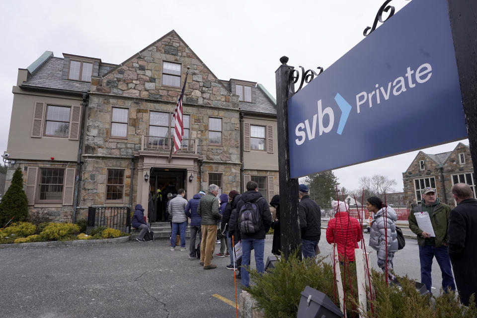 Customers and bystanders form a line outside a Silicon Valley Bank branch location, Monday, March 13, 2023, in Wellesley, Mass. (AP Photo/Steven Senne)