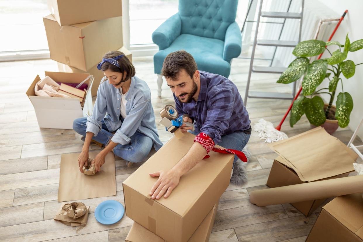 High angle view of a young couple in love sitting on the floor of their apartment, packing things into cardboard boxes, getting ready for relocation