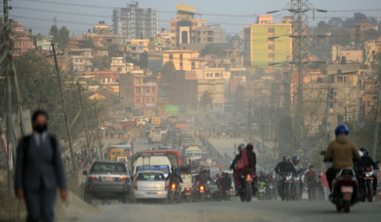 Vehicles and motorbike riders travel on a dusty road in Kathmandu