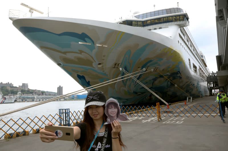 A woman takes a selfie in front of the Explorer Dream cruise ship, in Keelung