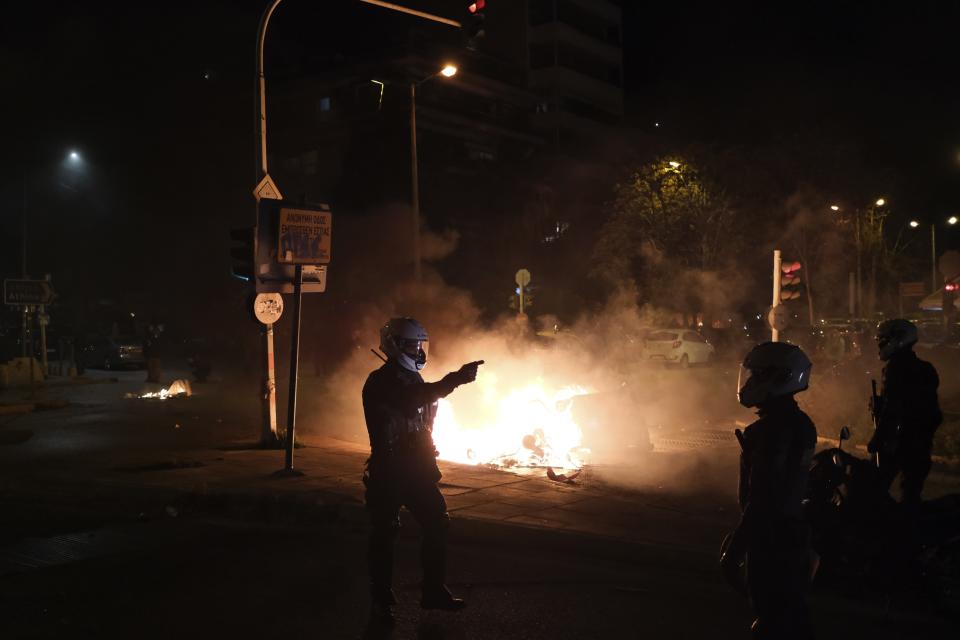 A policeman gestures as a recycle bin is on fire during clashes in Athens, Tuesday, March 9, 2021. Severe clashes broke out Tuesday in Athens after youths protesting an incident of police violence attacked a police station with petrol bombs, and severely injured one officer. (AP Photo/Aggelos Barai)