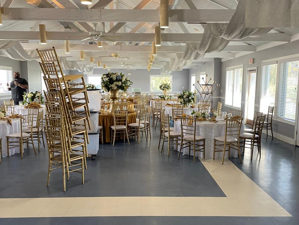 Several chairs stacked on top of each other with tables and more chairs arranged in a wedding venue