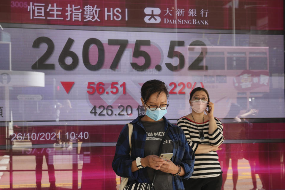 People wearing face masks walk past a bank's electronic board showing the Hong Kong share index in Hong Kong, Tuesday, Oct. 26, 2021. Asian shares were mostly higher Tuesday after another rally to a record high on Wall Street. (AP Photo/Kin Cheung)