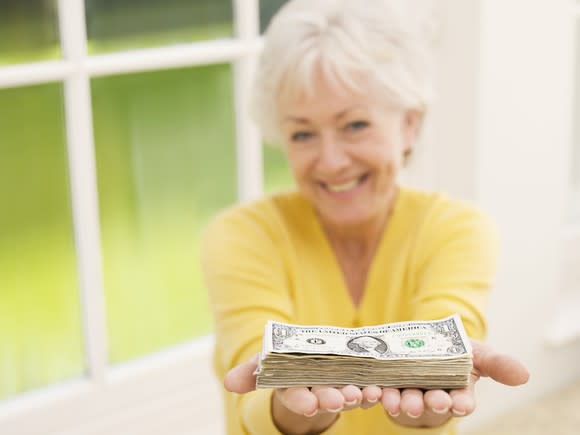 A senior woman holding a stack of cash in her outstretched hands.