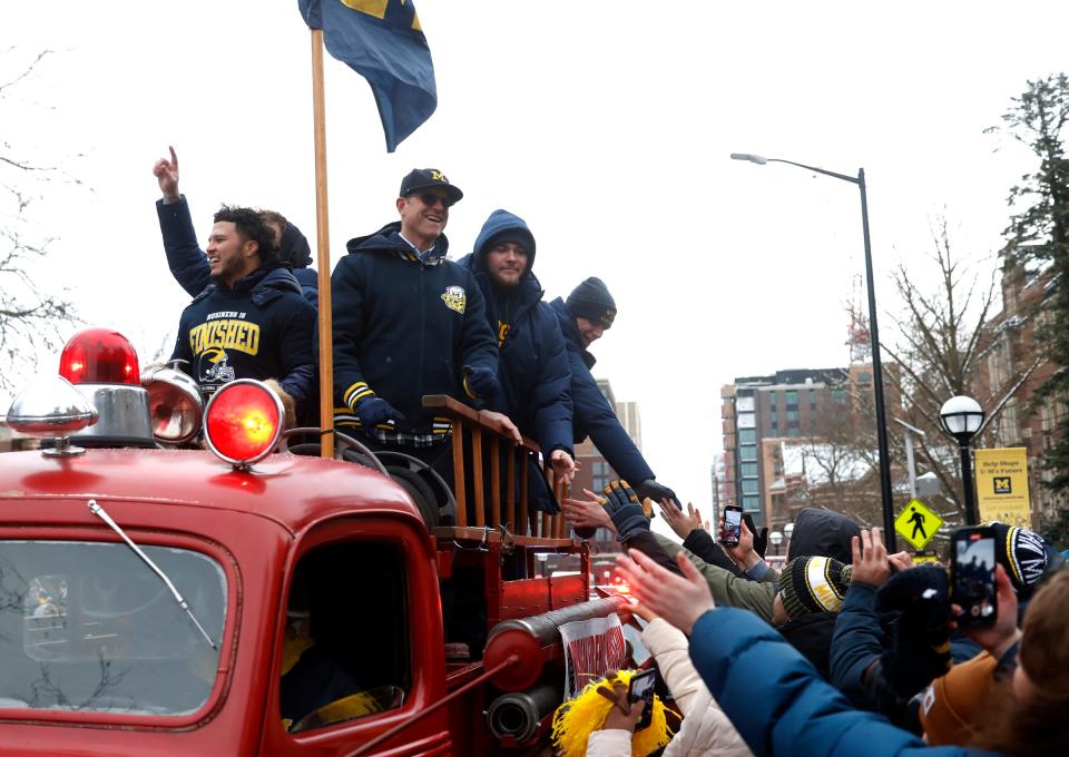 Michigan fans rush an old fire truck to shake hands with Michigan head football coach Jim Harbaugh and some of his star players as they head down South University Avenue during a parade for the newly crowned national champions on campus in Ann Arbor on Saturday, Jan. 13, 2024.