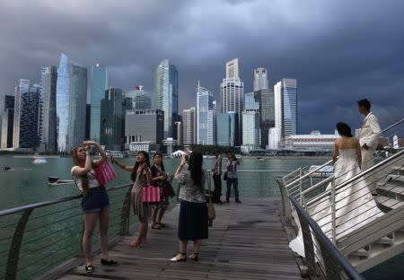 Tourists and a wedding couple from overseas take photos along the Marina Bay in the backdrop of the financial district of Singapore March 9, 2015. REUTERS/Edgar Su