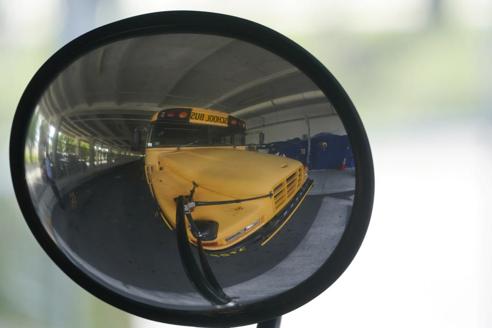 A diesel-powered school bus is reflected in a mirror at MAST Academy, Wednesday, Sept. 29, 2021, in Miami. Student Holly Thorpe, 14, urged the Miami-Dade County Public Schools to considering replacing foul-smelling diesel school buses with electric vehicles. The school board voted this week to use a state grant to purchase up to 50 electric buses. Miami-Dade is joining a growing number of school districts transitioning from diesel to more environmentally-friendly electric school buses. (AP Photo/Wilfredo Lee)