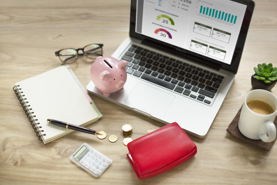 Piggy bank, laptop, purse with money, coffee cup on wooden table top.