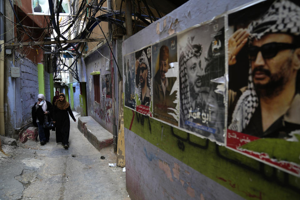 Palestinian women pass next of portraits of the late Palestinian leader Yasser Arafat, in an alley at the Bourj al-Barajneh Palestinian refugee camp, in Beirut, Lebanon, Tuesday, Jan. 18, 2022. The agency for Palestinian refugees, or UNRWA, appealed Wednesday to the international community to donate tens of millions of dollars to help improve living conditions for Palestinians in crisis-hit Lebanon. UNWRA is asking for an additional $87.5 million to provide Palestinian refugees with cash assistance to the poorest, cover hospital expenses, as well as transportation for children so that they can go to school. (AP Photo/Hussein Malla)