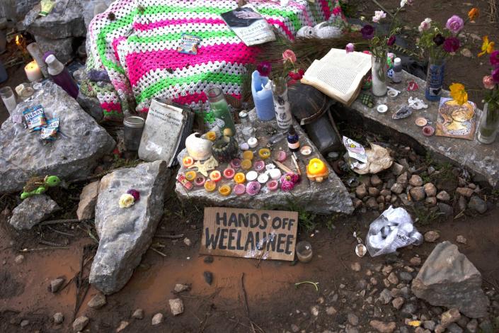 A cardboard sign near candles and rocks reads 