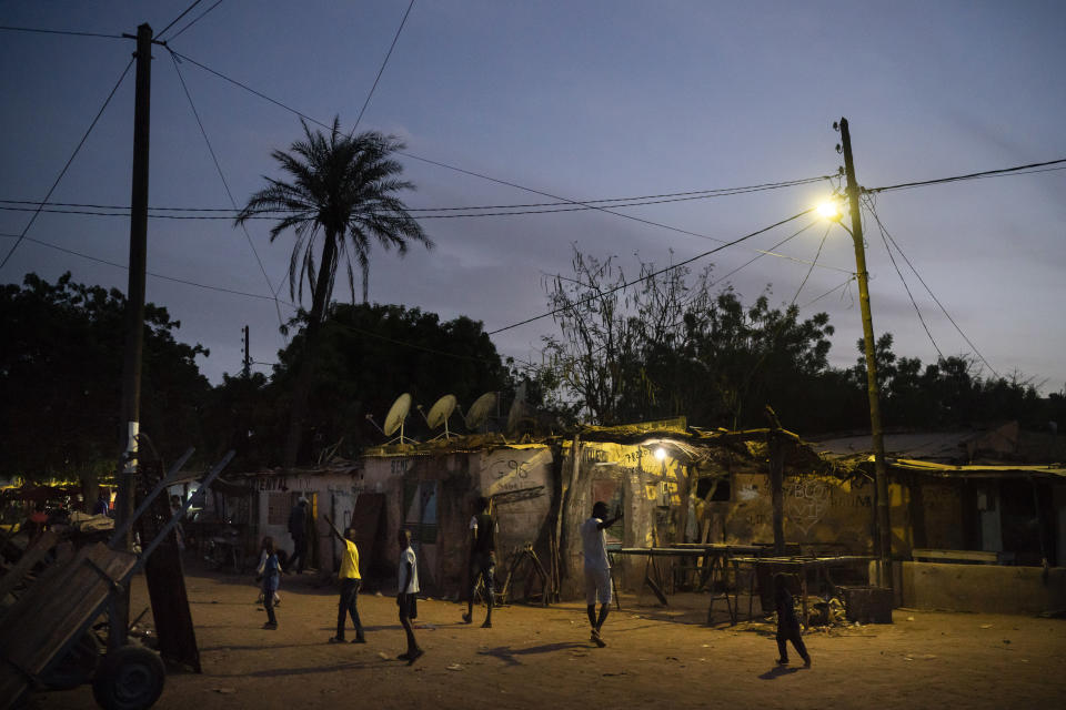 In this Nov. 25, 2018 photo, people walk down a street at dusk in Goudiry, Senegal. Many of the victims of the 2015 shipwreck are believed to have come from the Tambacounda region of Senegal, where economic prospects are few and many toil in agriculture despite growing desertification and a lack of modern farming equipment. (AP Photo/Felipe Dana)