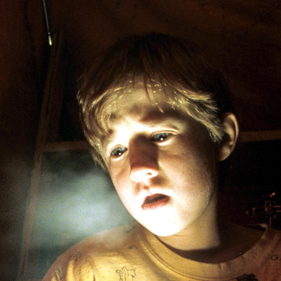 Haley Joel Osment as Cole Sear, illuminated by a flashlight, with a curious expression in a dark room, from the movie 