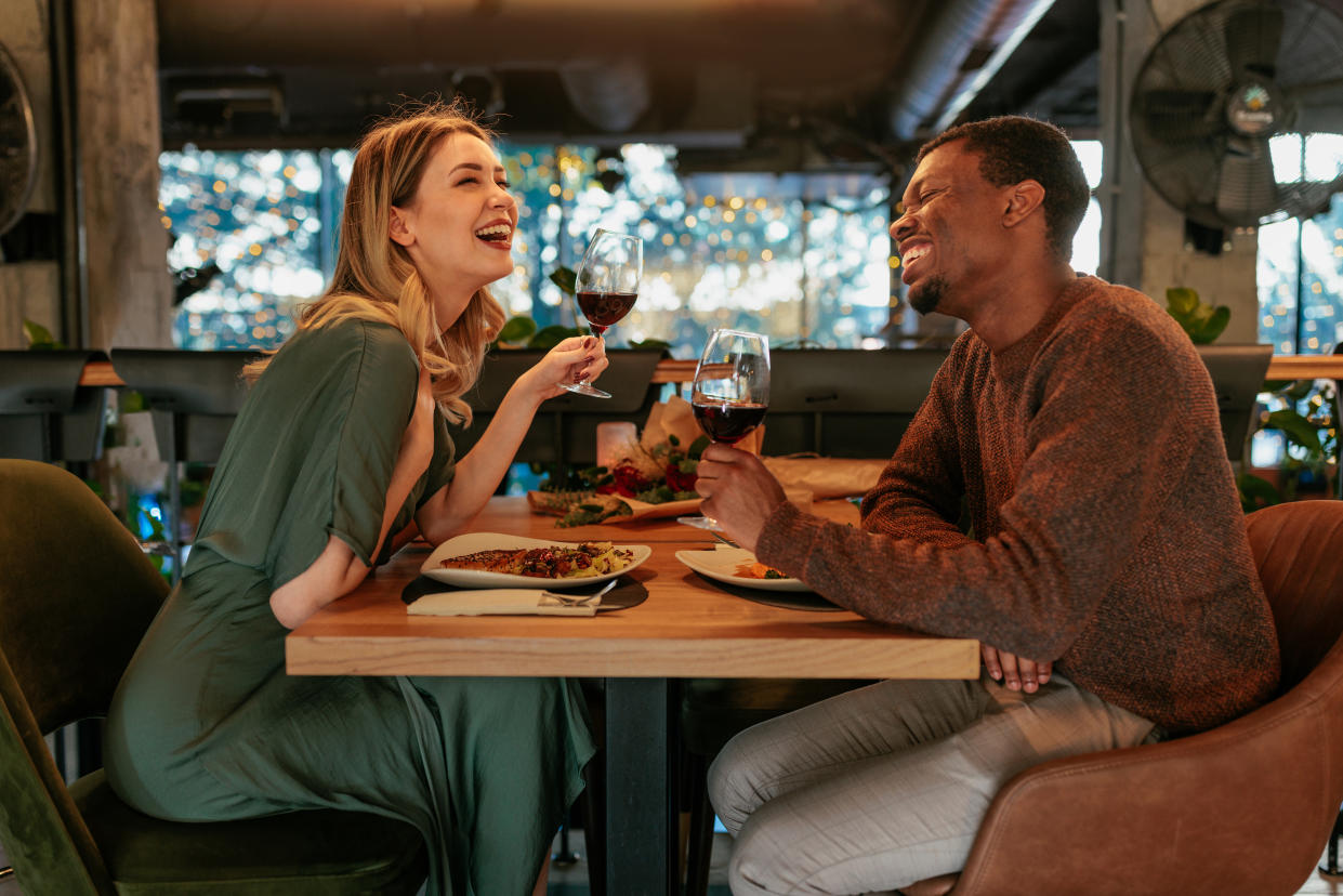 A young multiethnic couple is smiling and talking while enjoying wine and food in a restaurant.