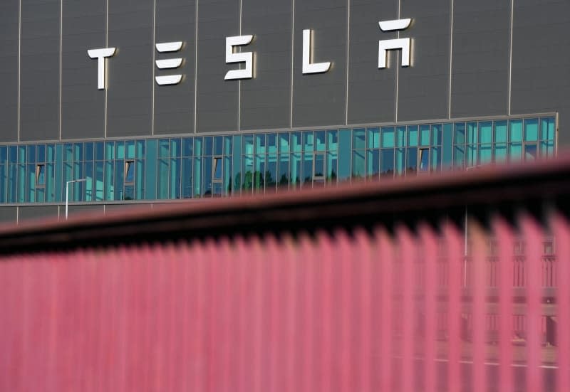 The lettering "Tesla" is on the façade of a Tesla Gigafactory building. The railings of the bridge on the L38 road can be seen in the foreground. On 16 May, municipal representatives from Gruenheide approved a development plan that clears the way for an expansion of the Tesla factory. The car manufacturer wants to expand its site to include a freight yard and logistics areas. Soeren Stache/dpa