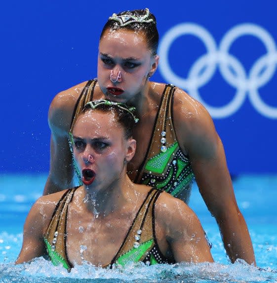 Two ferocious-looking swimmers, one in the water at chest height and the other behind and above her, seeming to rest her chin on the other swimmer's head