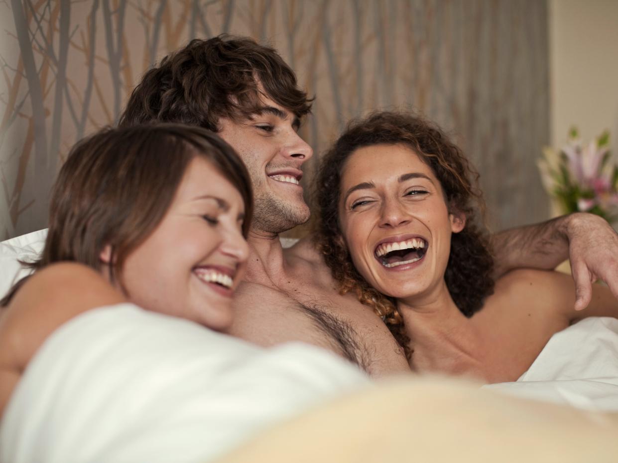 Smiling man lying with women in bed at home