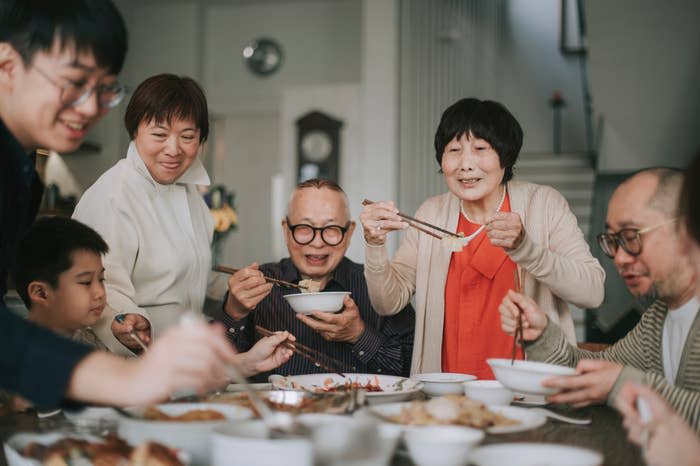 A family gathered around a table enjoying a meal together, using chopsticks and sharing dishes. Faces express joy and warmth during the dining experience