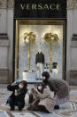 Tourists, wearing face masks, pose for a selfie in front of a Versace shop window in downtown Milan, Italy, Thursday, Feb. 27, 2020. In Europe, an expanding cluster in northern Italy is eyed as a source for transmissions. (AP Photo/Luca Bruno)