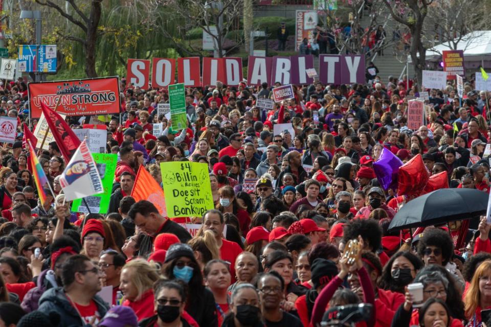 Huge crowd gather at a downtown park, many in red shirts.