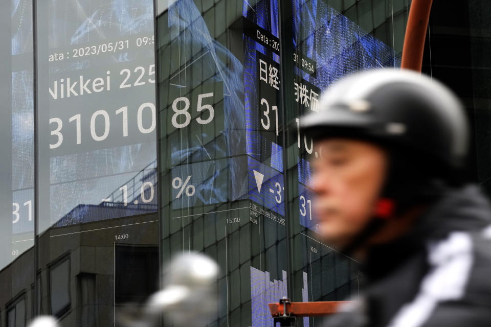 A person rides a moped near an electronic stock board showing Japan's Nikkei 225 index at a securities firm Wednesday, May 31, 2023, in Tokyo. Asian stock markets sank Wednesday ahead of a vote by Congress on a deal to avert a government debt default, while a downturn in Chinese factory activity deepened, adding to signs global economic activity is weakening. (AP Photo/Eugene Hoshiko)