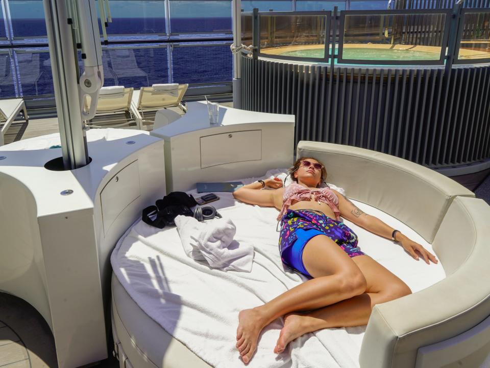 The author lays on a white bed on a cruise ship deck with a plunge pool behind her.