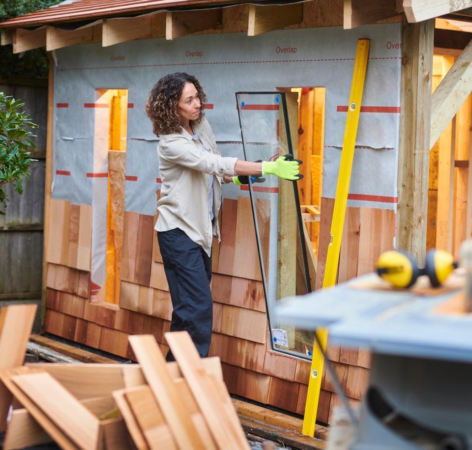 Woman installing windows into shed that is under construction