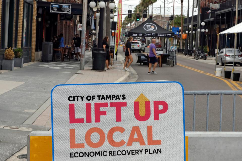 Pedestrians walk along a closed stretch of 7th AVe., in Ybor City Sunday, May 10, 2020, in Tampa, Fla. City officials have closed part of the road to allow restaurants to setup tables to help boost Tampa's economy and spread up recovery from the effects of the coronavirus.