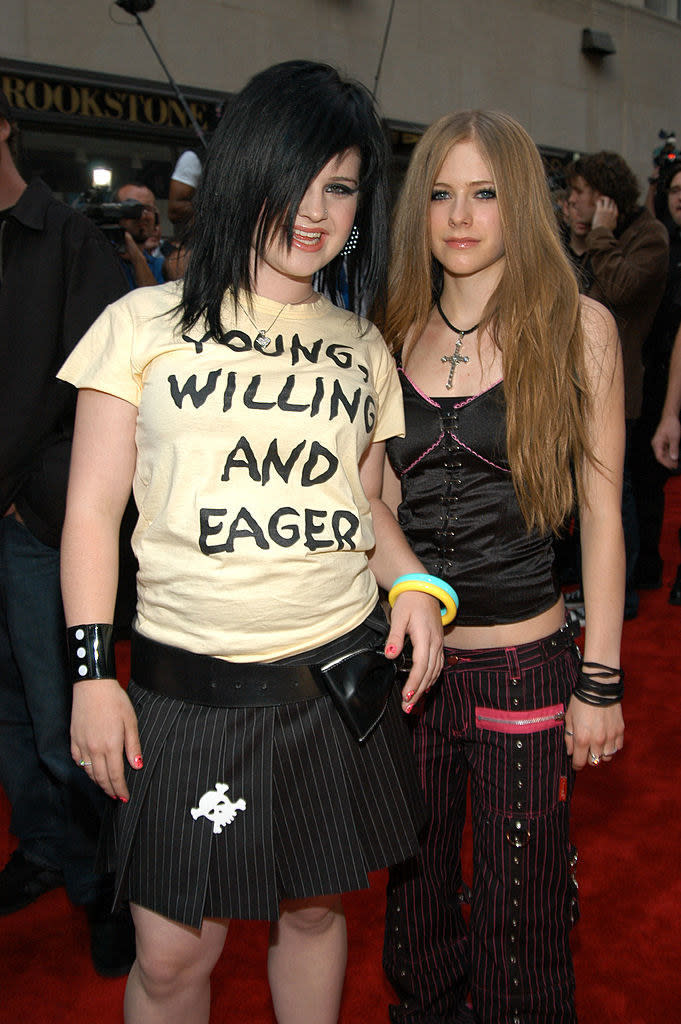 Kelly is wearing a pinstripe black skirt with a skull on it and a shirt that says "young, willing, and eager;" Avril is wearing black pinstripe pants