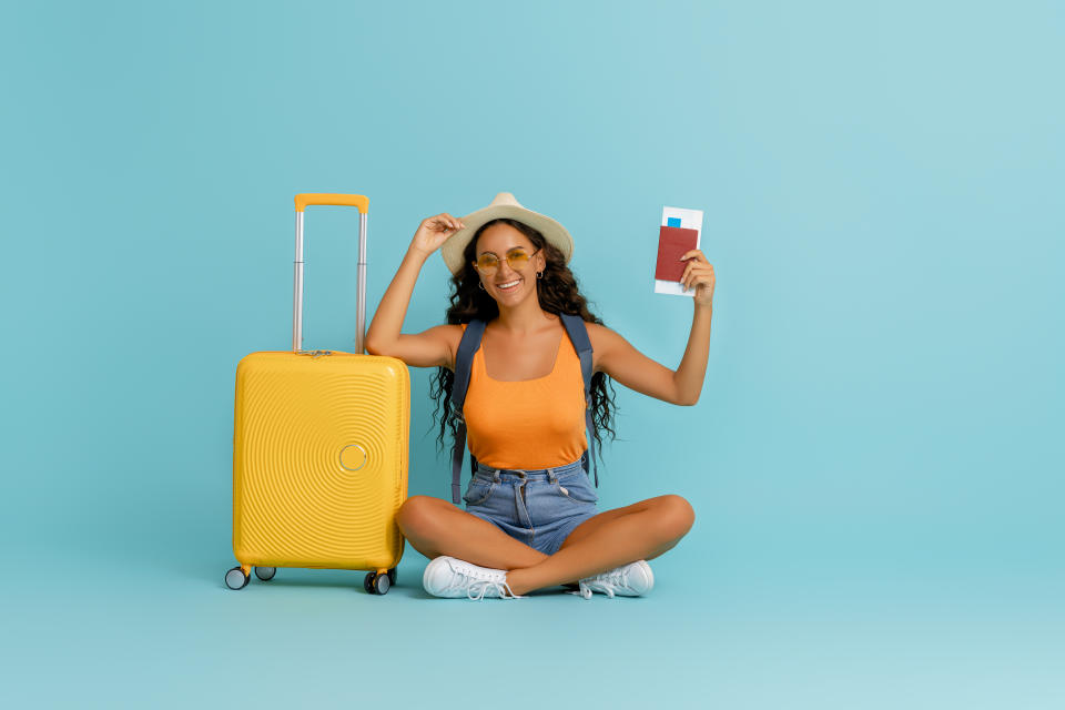 Go on an adventure! Happy woman going traveling. Young person with suitcase on color teal background.