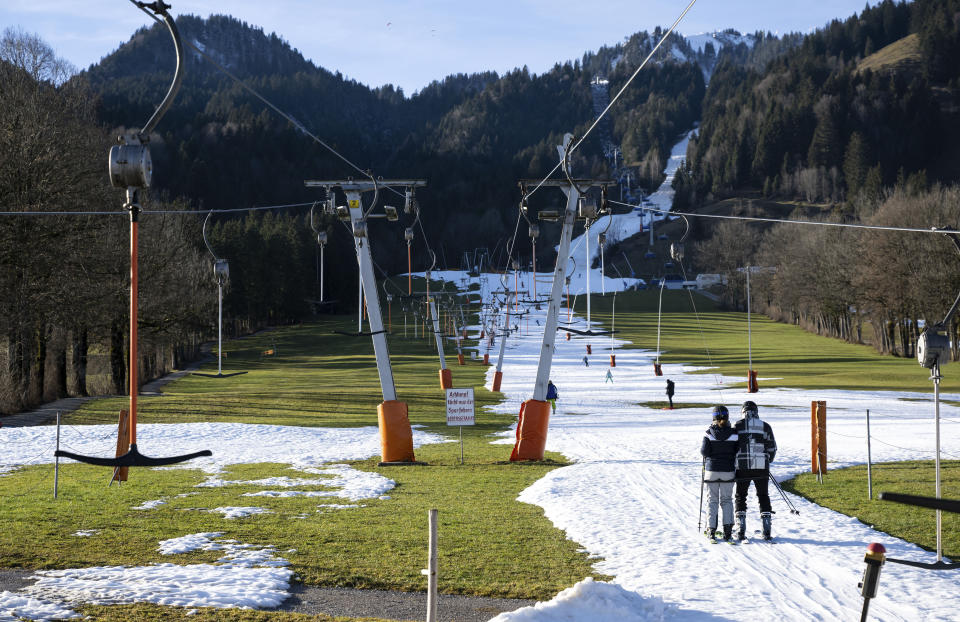 People ski up the slope on the Draxlhang in the Brauneck ski area using a T-bar lift in Lenggries, Germany, Wednesday, Dec. 28, 2022. Sparse snowfall and unseasonably warm weather in much of Europe is allowing green grass to blanket many mountaintops across the region where snow might normally be. It has caused headaches for ski slope operators and aficionados of Alpine white this time of year. (Sven Hoppe/dpa via AP)