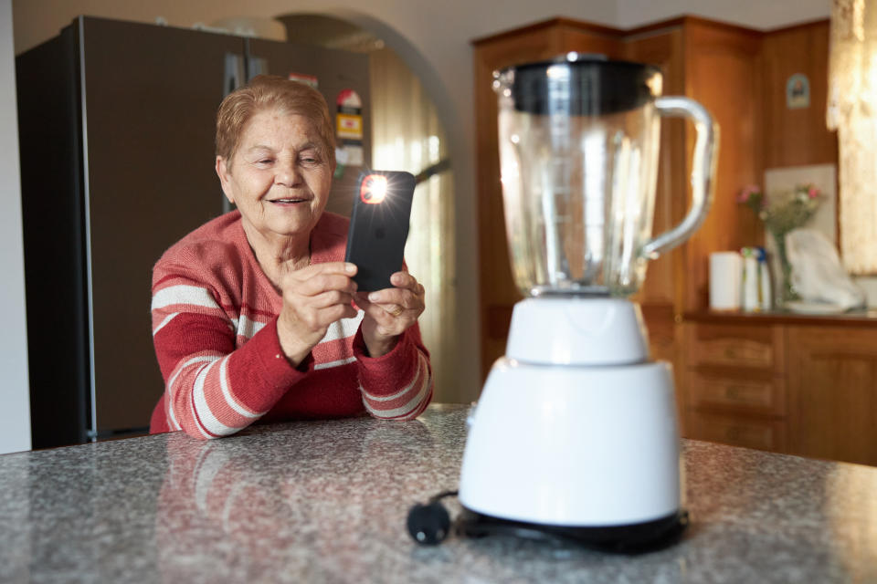 Lady taking a photograph of a blender with her smart phone.