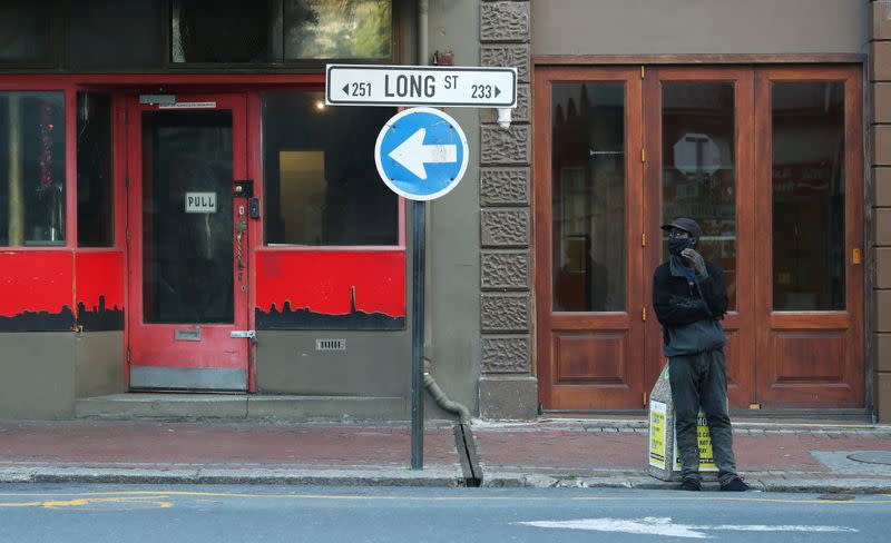 An informal car-guard stands before a closed bar and restaurant in Long Street in Cape Town