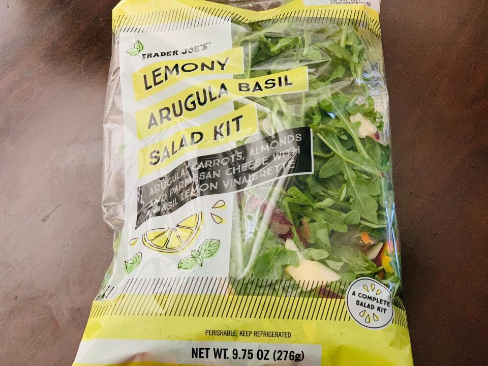 Trader Joe's lemony arugula salad kit in clear and yellow bag on a dark wood table