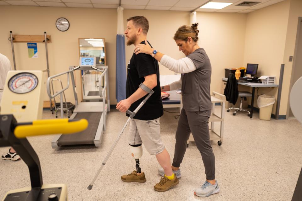 A soldier with a prosthetic leg is assisted inw alking by a physical therapist