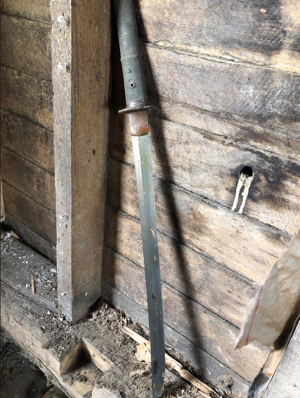 Old sword leaning against a wooden wall inside a dusty shed