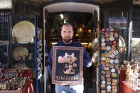 Adnan Hidic poses for a photo with the copper souvenir depicting Sarajevo Winter Olympics mascot Vucko in front of his shop in the old town Bascarsija, in Sarajevo, Bosnia, Monday, Feb. 5, 2024. Sarajevo is paying tribute this week to one of its most glorious moments: the two weeks of February in 1984 when it staged an impeccable Winter Olympic Games. While taking the nostalgic trip down memory lane, Bosnian Olympians say they are looking to the future with hope to again pull off an “apparently impossible feat” and reignite the Olympic flame over Sarajevo in 2032. (AP Photo/Armin Durgut)