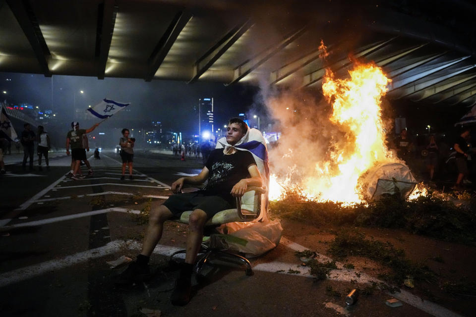 A demonstrator sits next to a bonfire as others occupy the Ayalon Highway to protest against plans by Prime Minister Benjamin Netanyahu's government to overhaul the judicial system in Tel Aviv, Thursday, July 20, 2023. (AP Photo/Ariel Schalit)