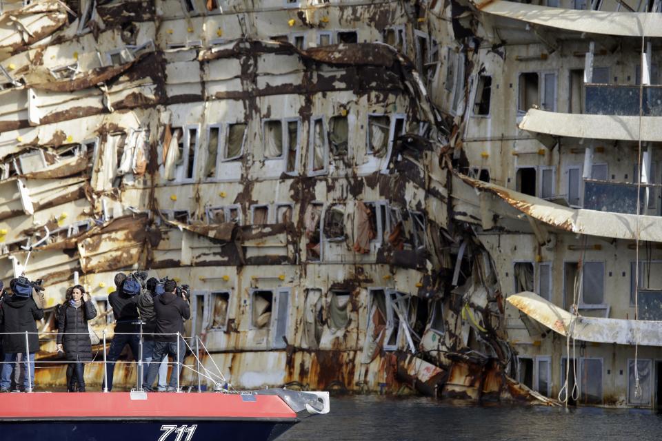 Journalists film the previously submerged side of the Costa Concordia cruise ship off the coast of the Tuscan Island of Giglio, Italy, Monday, Jan. 13, 2014. Survivors of the capsized Costa Concordia are commemorating the second anniversary of the grounding off Tuscany that killed 32 people. The Concordia slammed into a reef off Giglio when the captain took it off course in an apparent stunt to bring it closer to the island. With a 70-meter (230-foot) gash in its hull, the ship listed for an hour and finally capsized off Giglio's port. (AP Photo/Gregorio Borgia)