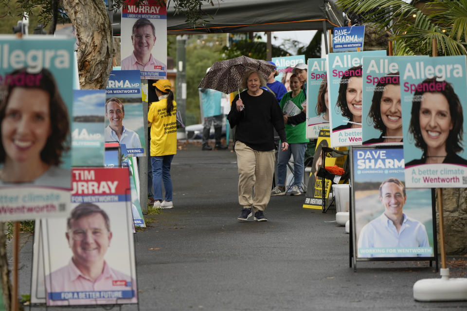 A woman walks past billboards for candidates outside a polling station in Sydney, Australia, Monday, May 9, 2022. Early voting has begun in Australia's federal election with the opposition party hoping the first ballots will reflect its lead over the government in an opinion poll. (AP Photo/Mark Baker)