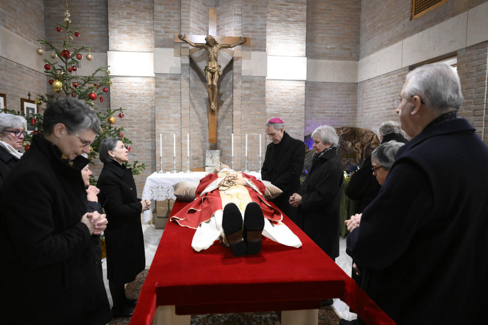 In this image released on Monday, Jan. 2, 2023, by the Vatican Media news service, Bishop George Gaenswein, center, and close entourage pray in front of the body of late Pope Emeritus Benedict XVI lying out in state in the chapel of the monastery 'Mater Ecclesiae' where he mostly lived after retiring on Feb. 28, 2013. Pope Benedict, the German theologian who will be remembered as the first pope in 600 years to resign, has died, the Vatican announced Saturday, Dec. 31, 2022. He was 95. (Vatican Media via AP)