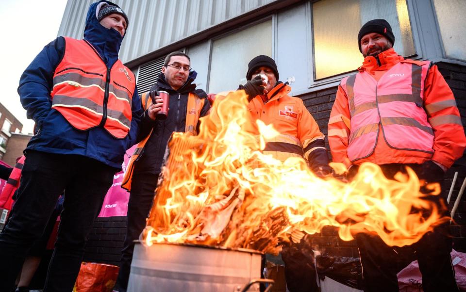 A group of striking postal workers stand around a fire as they picket outside a Royal Mail sorting office on December 14, 2022 in London - Leon Neal/Getty Images