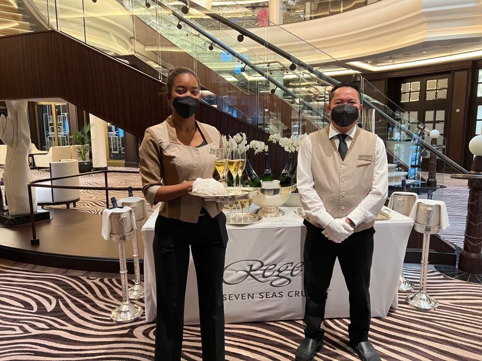 two masked cruise workers posing for a photo in front of a champagne welcome table on a cruise