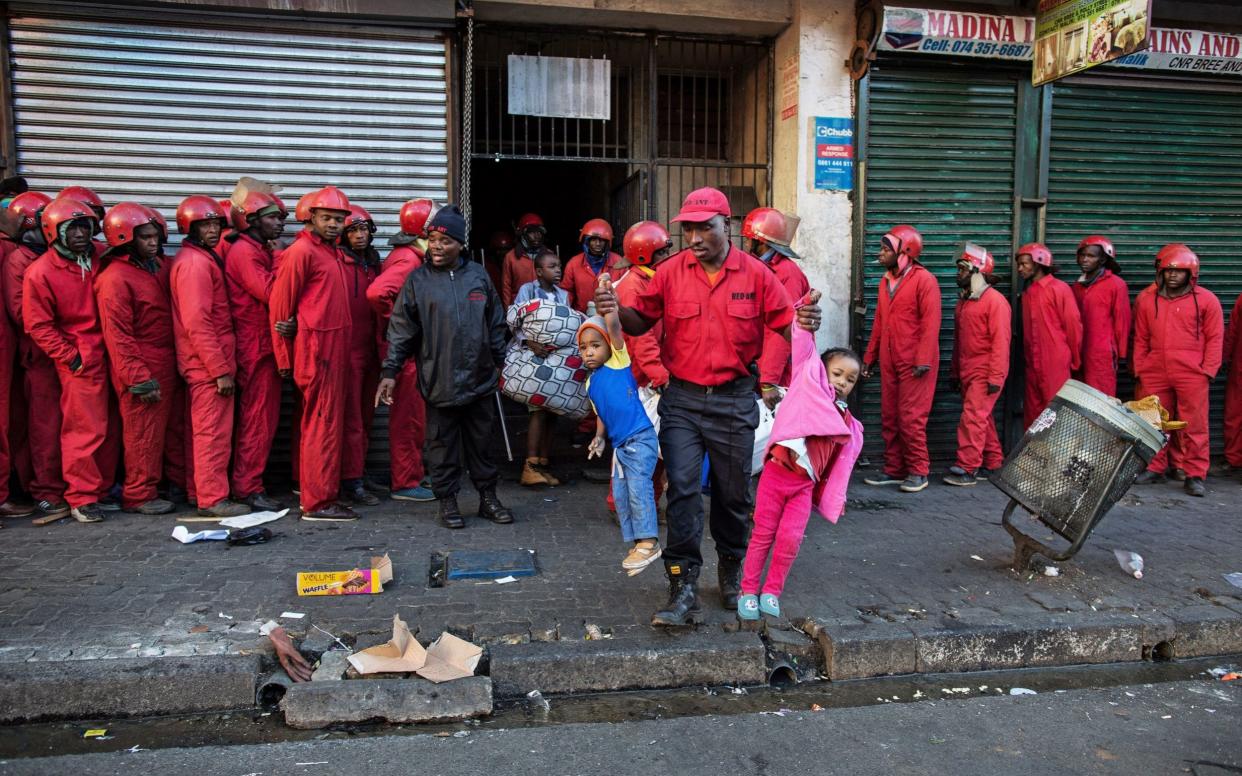 A Red Ants major carries out two small children during the eviction of residents of a so-called hijacked building in Bree Street, Johannesburg - James Oatway