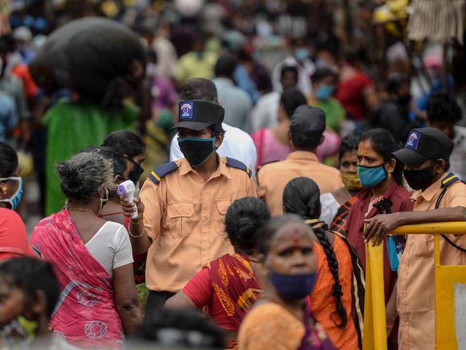 A security personnel (C) checks the body temperature of a woman (C-L) as she enters a market among a crowd of people as a preventive measure against the spread of the COVID-19 coronavirus in Chennai on July 29, 2020. (Photo by Arun SANKAR / AFP) (Photo by ARUN SANKAR/AFP via Getty Images)