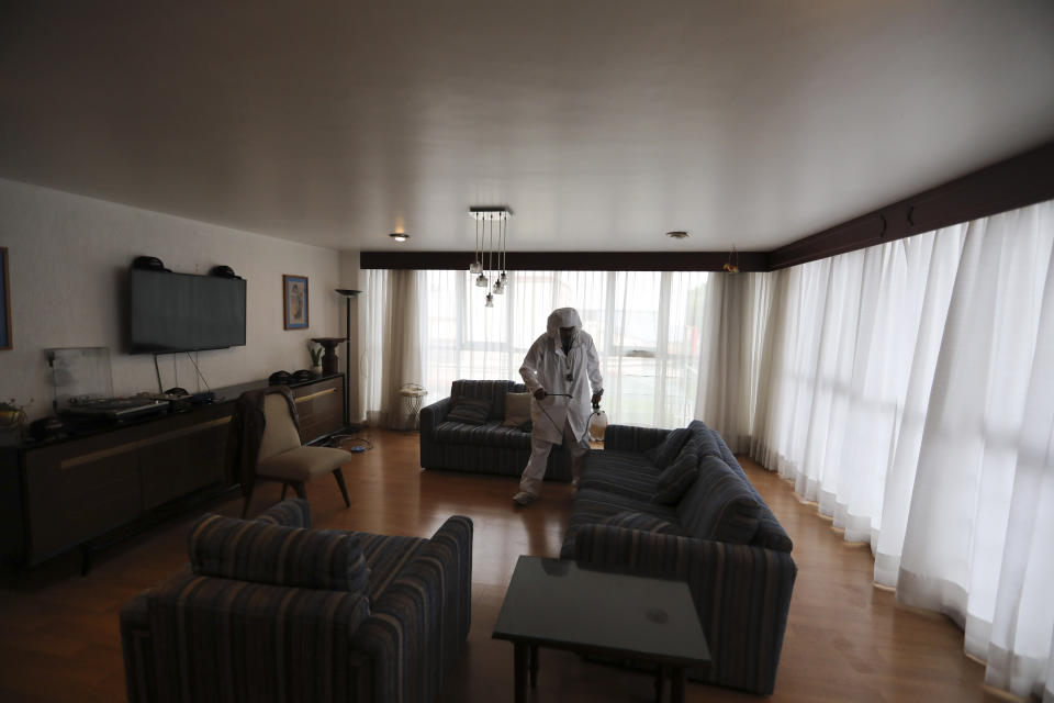 A worker sprays a living room with disinfectant in preparation for dancers performing in a client's home in Mexico City, Saturday, Aug. 8, 2020. The pandemic has forced business to adapt to a new normality and the adult entertainment industry is no exception. After three months of inactivity, Mi Ultimo Beso relaunched his table-dance-at-home service observing health measures. (AP Photo/Eduardo Verdugo)